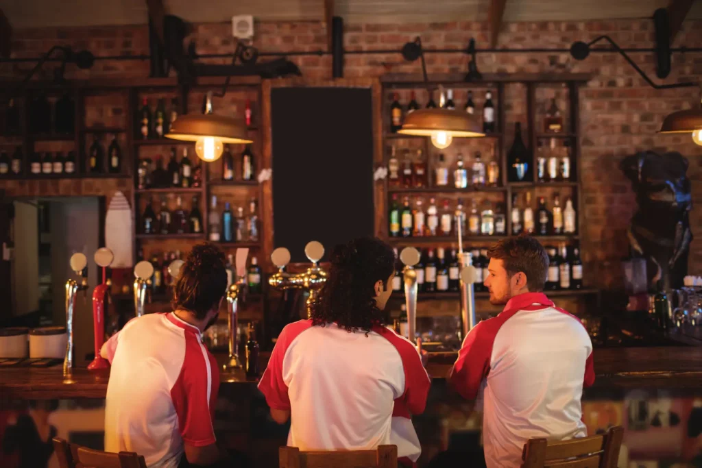 Clientes viendo un partido de fútbol en un pub con música ambiental